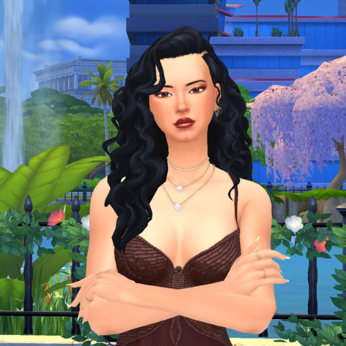 A female Sim wearing Sims 4 CC wavy long hair poses in a park. She has very voluminous wavy/curly hair with a deep side part